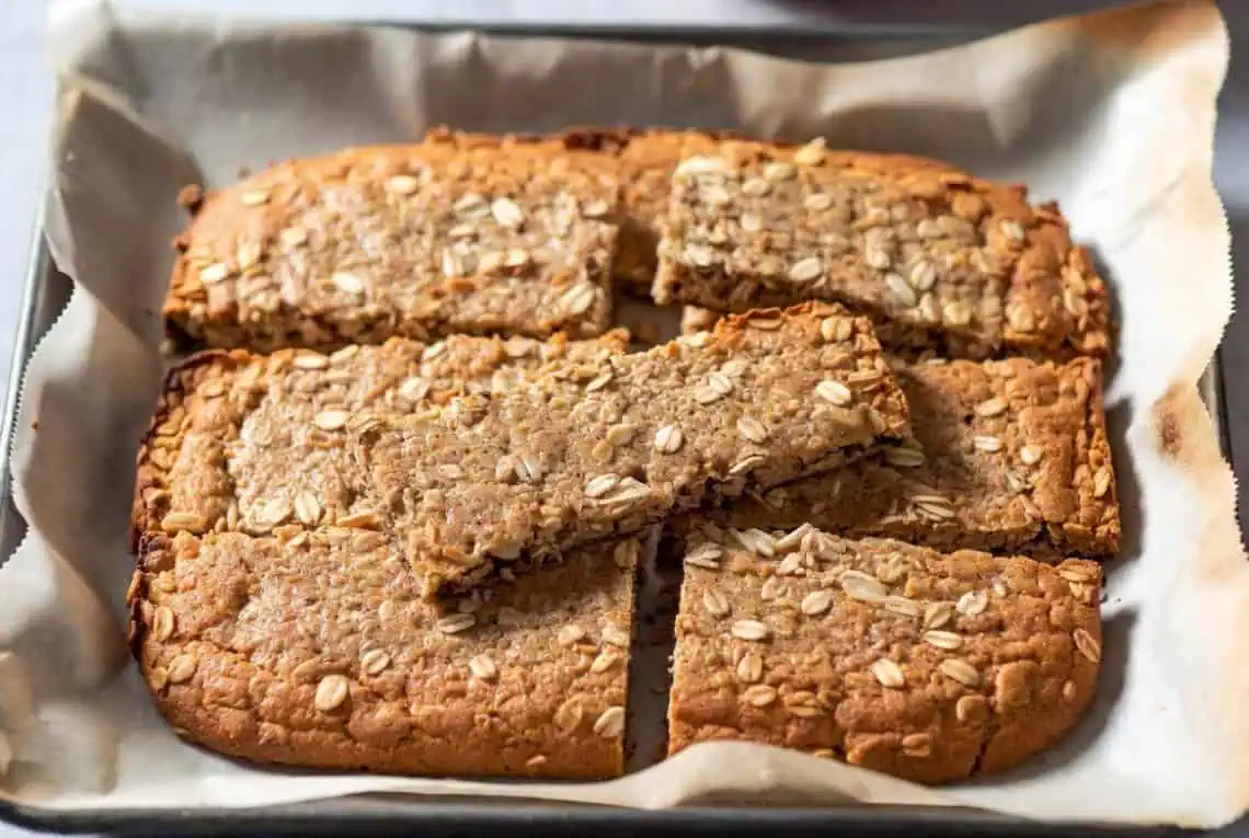 Oat-topped baked bars cut into squares on a parchment-lined baking sheet.