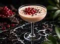 Amarula Cocktail - Saffarazzi Pale pink cocktail in a coupe glass, topped with pomegranate seeds and chocolate shavings on a dark marble surface.