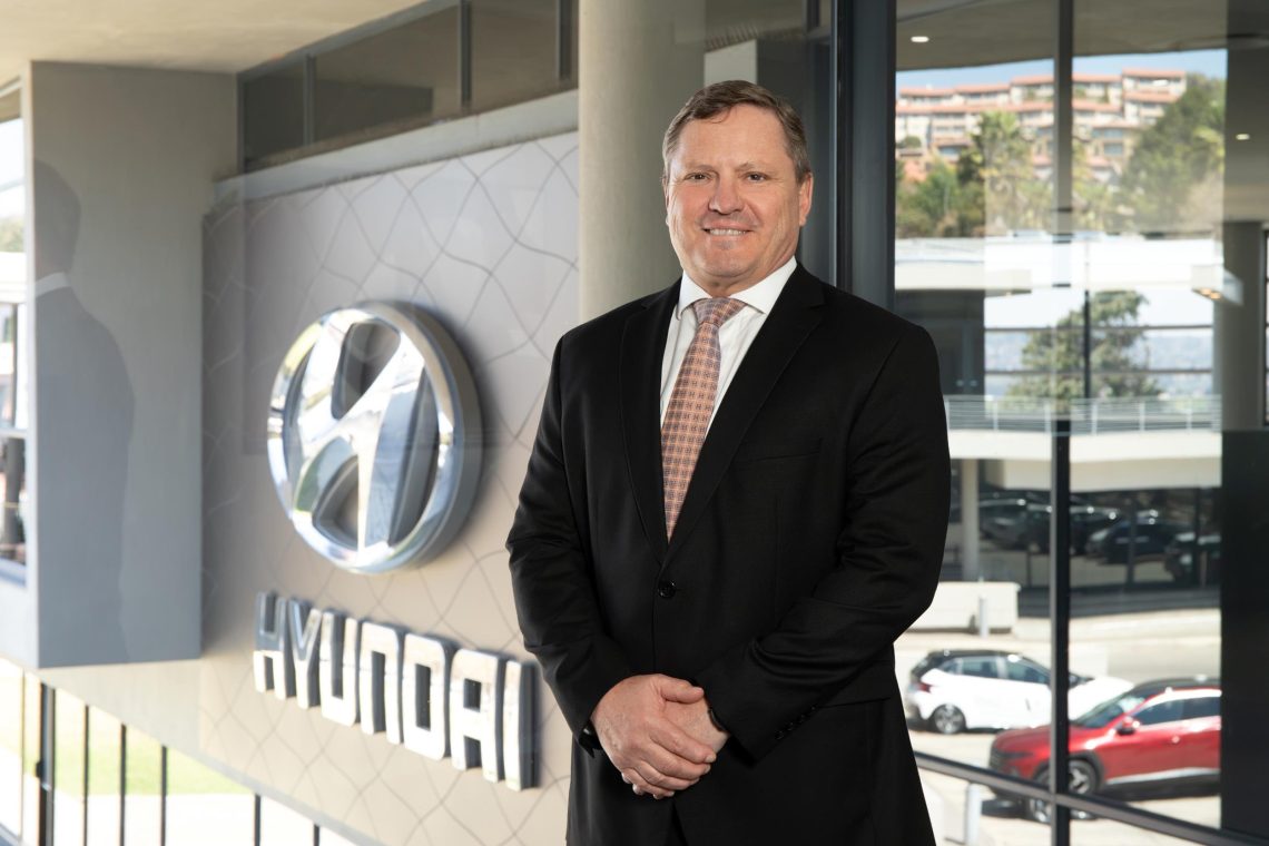 Hyundai executive standing beside logo at dealership showroom - Saffarazzi Hyundai executive standing beside logo at dealership showroom