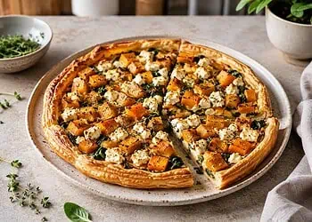 Savory puff pastry tart topped with roasted butternut, spinach and feta, cut into slices on a plate