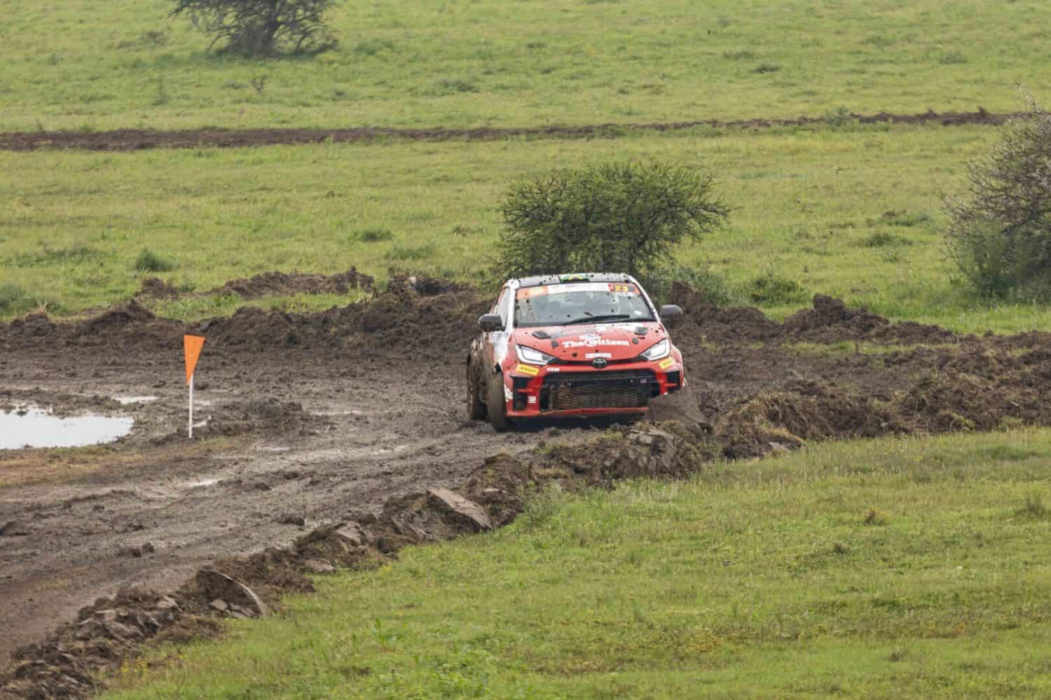 Toyota GR Yaris rally car through muddy bend near flag - Saffarazzi Toyota GR Yaris rally car through muddy bend near flag