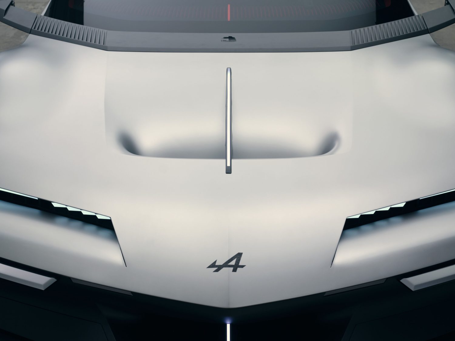 Alpine A310 Vision concept bonnet and badge detail - Saffarazzi Front view of a white sports car hood with a vertical chrome stripe running down the center and a small emblem above it within the windshield area.