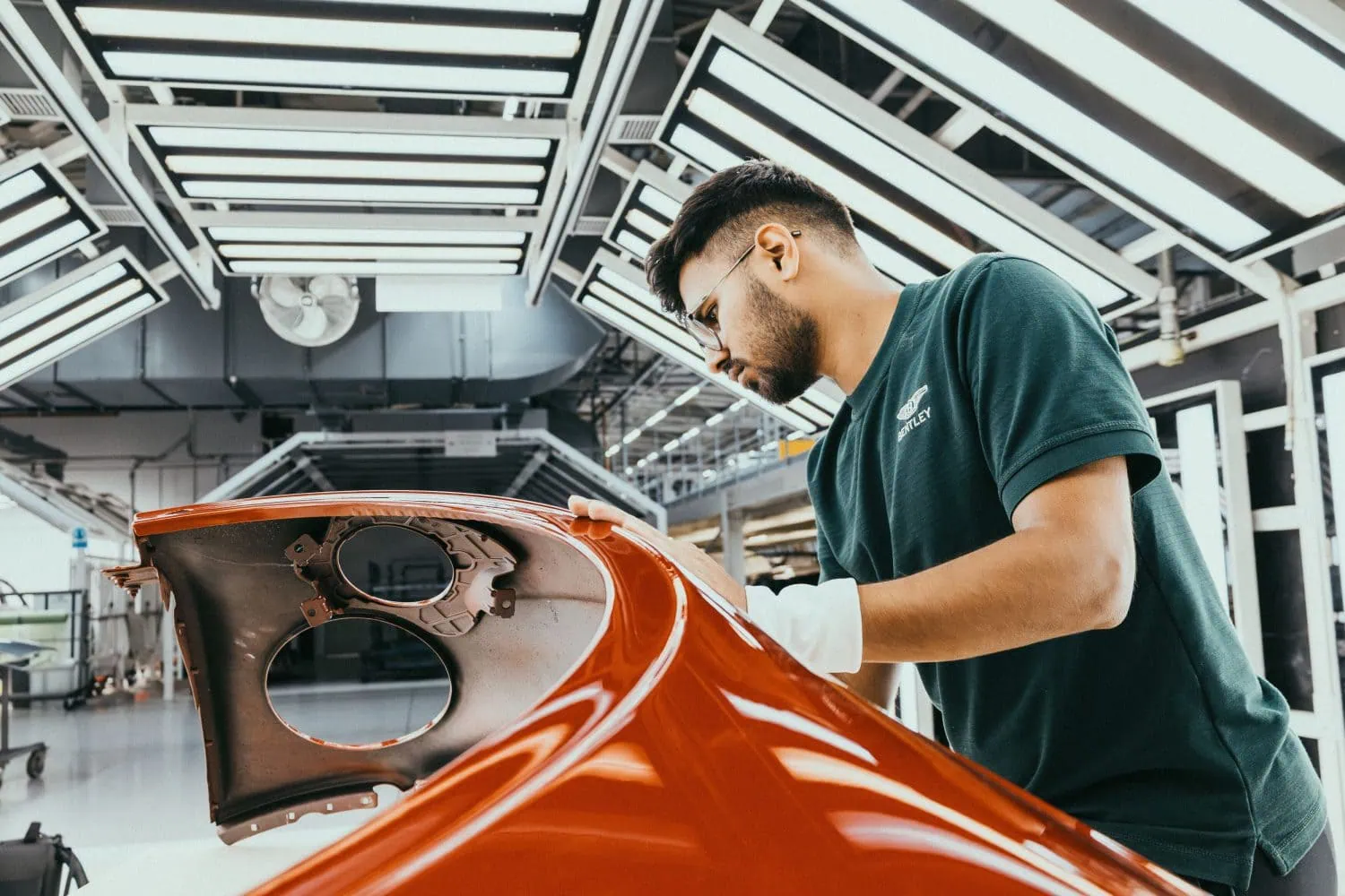 Bentley apprentice inspecting orange body panel in paint shop - Saffarazzi Bentley apprentice inspecting orange body panel in paint shop