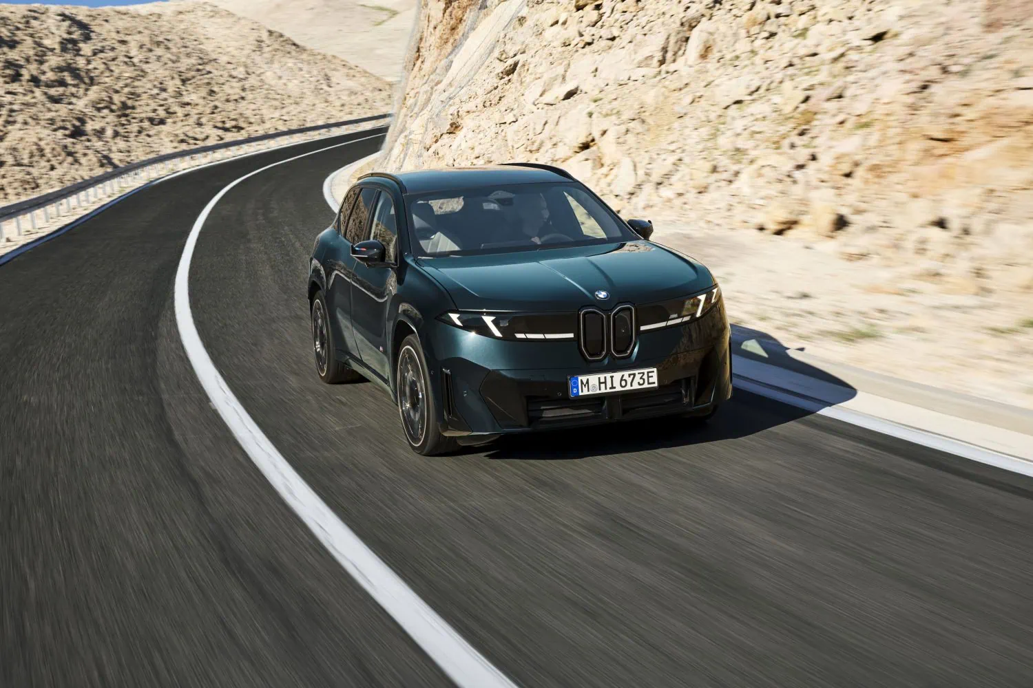 BMW iX3 M60 xDrive cornering past rocky hillside - Saffarazzi BMW iX3 M60 xDrive cornering past rocky hillside