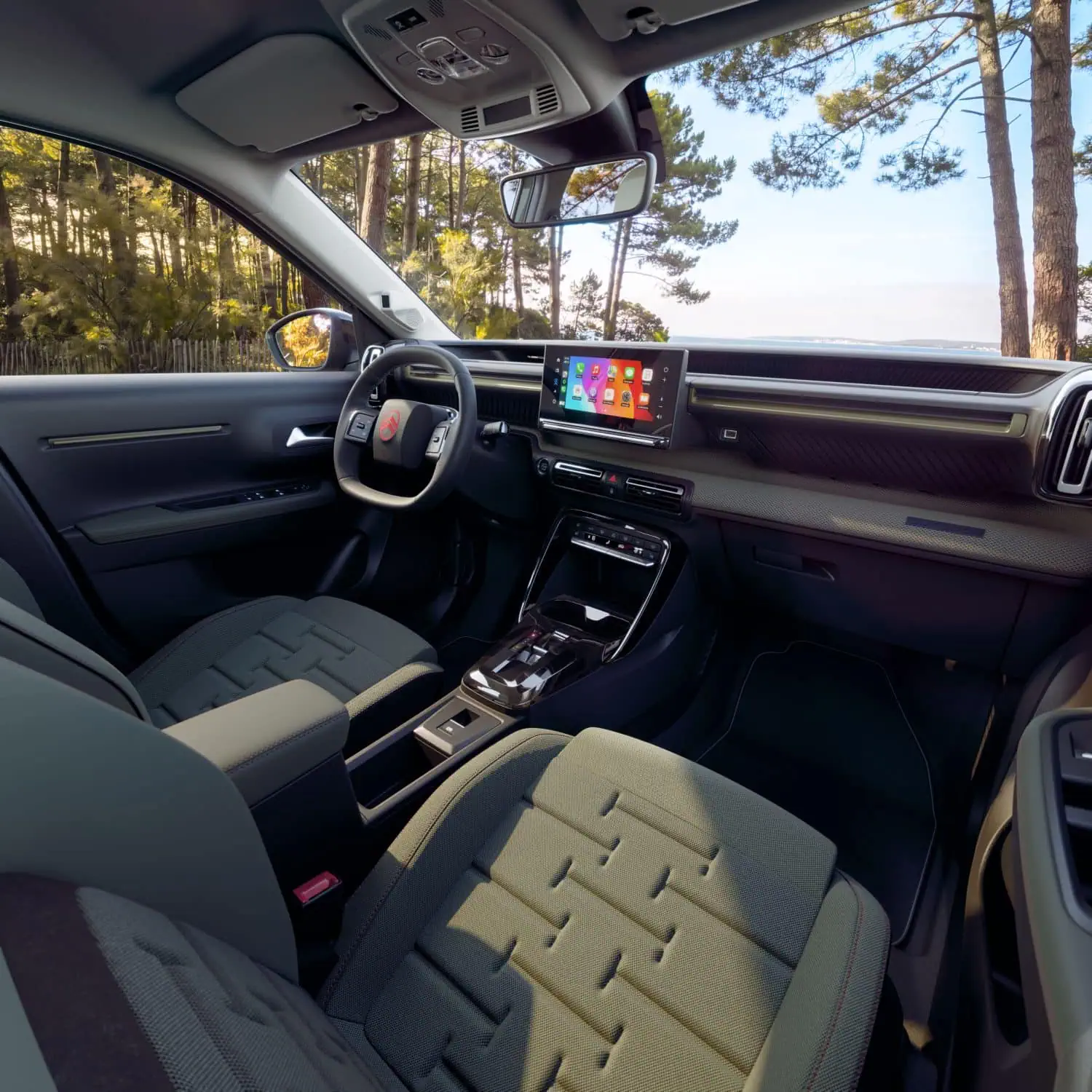 Citroën C3 OUTDOOR interior and dashboard - Saffarazzi Modern car interior with a large touchscreen display on the center console and a rearview mirror, forested scenery outside the side window.