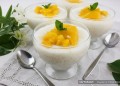 Glass cups of creamy coconut sago pudding topped with chopped mango on a summer table setting.