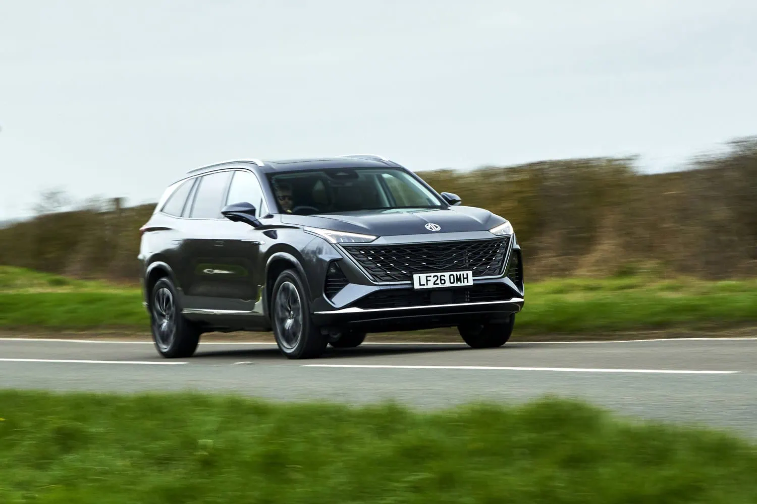 Dark grey MG S9 driving - Saffarazzi Dark grey MG S9 PHEV driving past hedgerow.