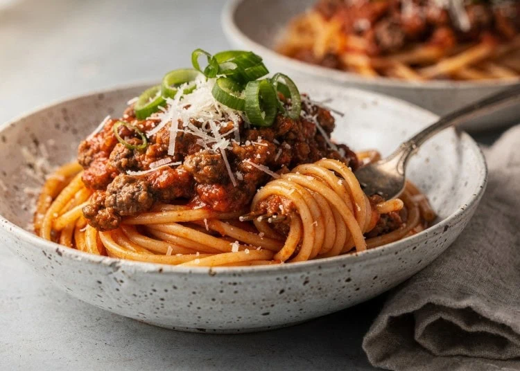 Easy Stovetop Spaghetti Bolognese - Saffarazzi Easy spaghetti bolognese topped with grated Parmesan and sliced spring onions in a speckled white bowl