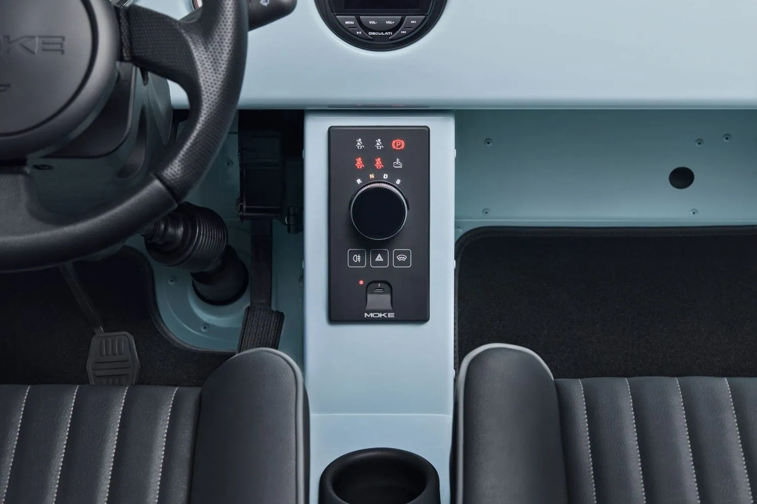 Electric MOKE Mk2 centre console between front seats - Saffarazzi Close-up of a car's center console with gear selector panel, cup holder, and part of the driver's seat and steering wheel.