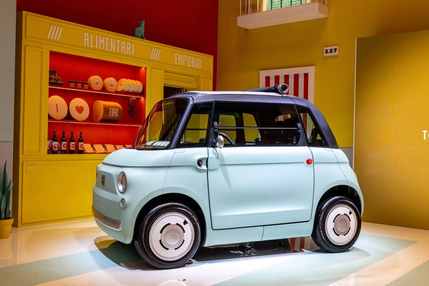 Fiat Topolino in light blue at shop display - Saffarazzi Light blue Fiat on display in a bright showroom with yellow shelves and a red wall.