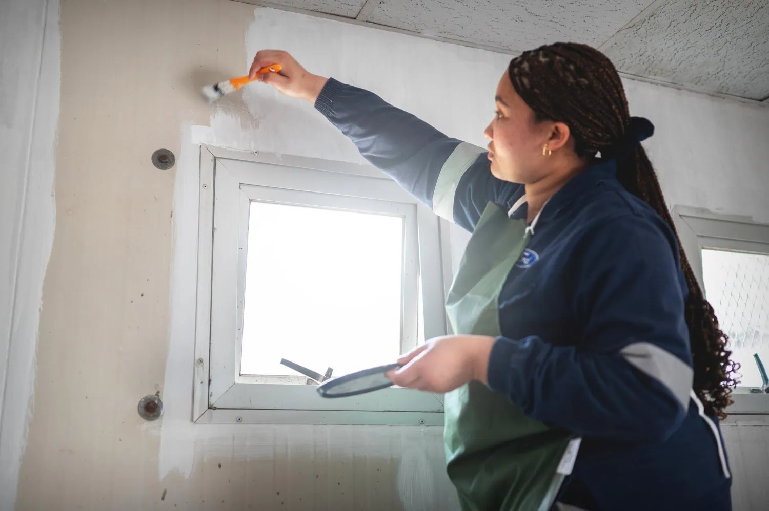 Volunteer painting interior wall - Saffarazzi Ford Global Caring volunteer painting a wall above a window.