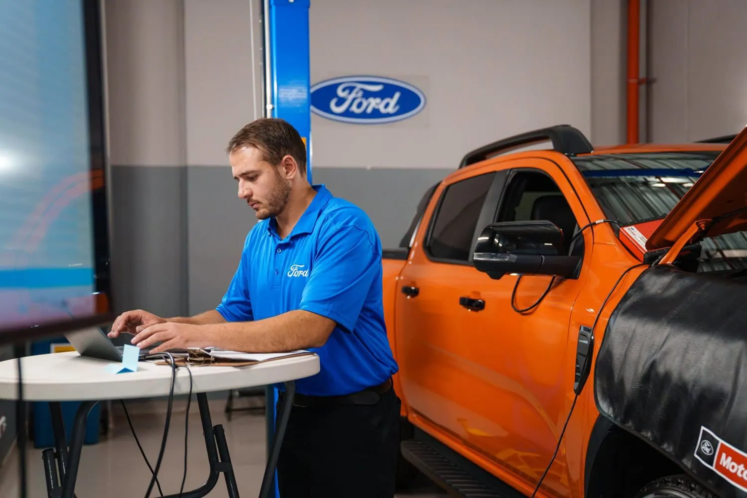 Technician at diagnostic laptop - Saffarazzi Ford technician using a laptop beside an orange Ranger.