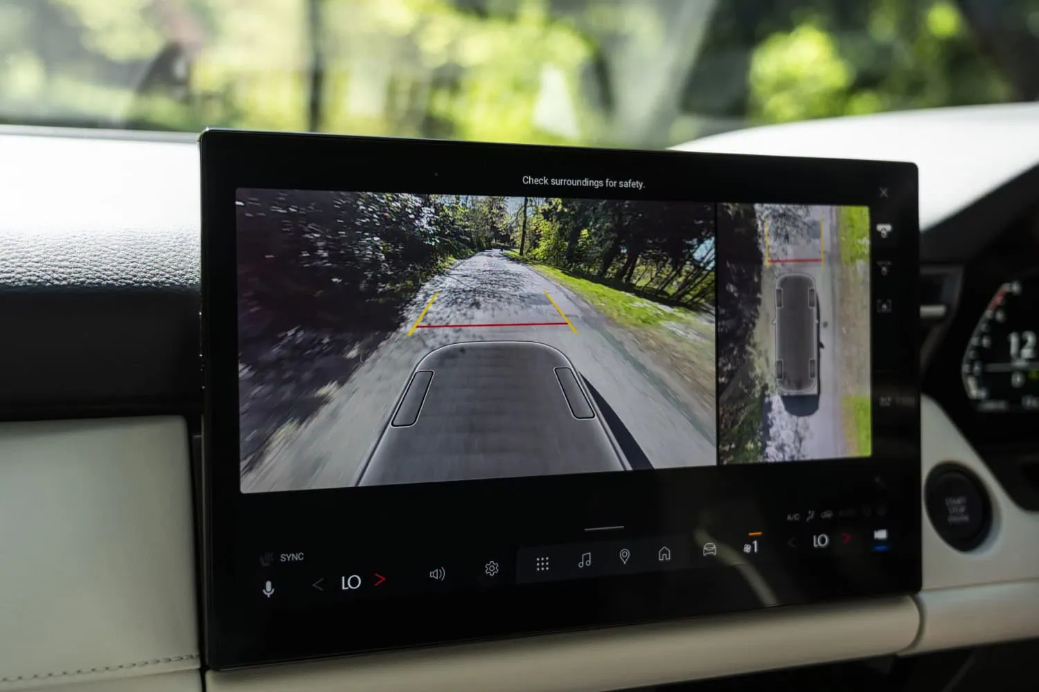 Mazda CX-5 camera display - Saffarazzi Rearview camera display showing a tree-lined road with yellow and red guiding lines for parking or reversing, on-screen safety note present.
