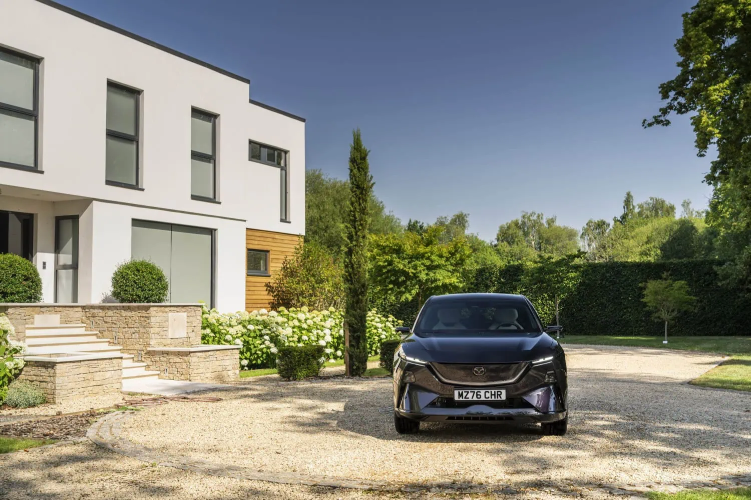 Mazda CX-6e press photo 3 - Saffarazzi Mazda CX-6e head-on view beside modern house.
