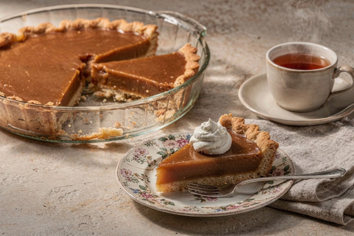 Microwave caramel yoghurt tart with a cut wedge and whipped cream beside a cup of tea