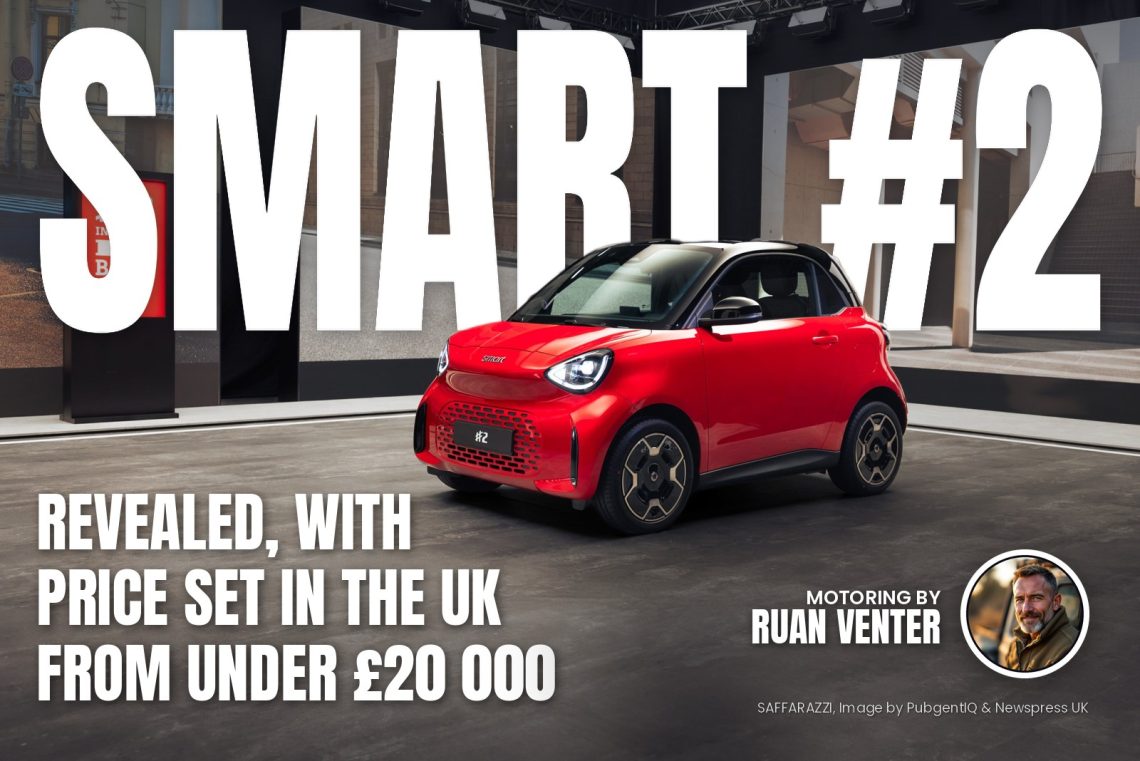 Red Smart car on display in a showroom with a city backdrop and overhead lighting rig.