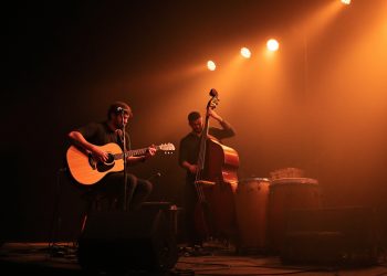Prime Circle Consider Me: Acoustic guitar player and upright bass on a dim stage under warm amber spotlights.