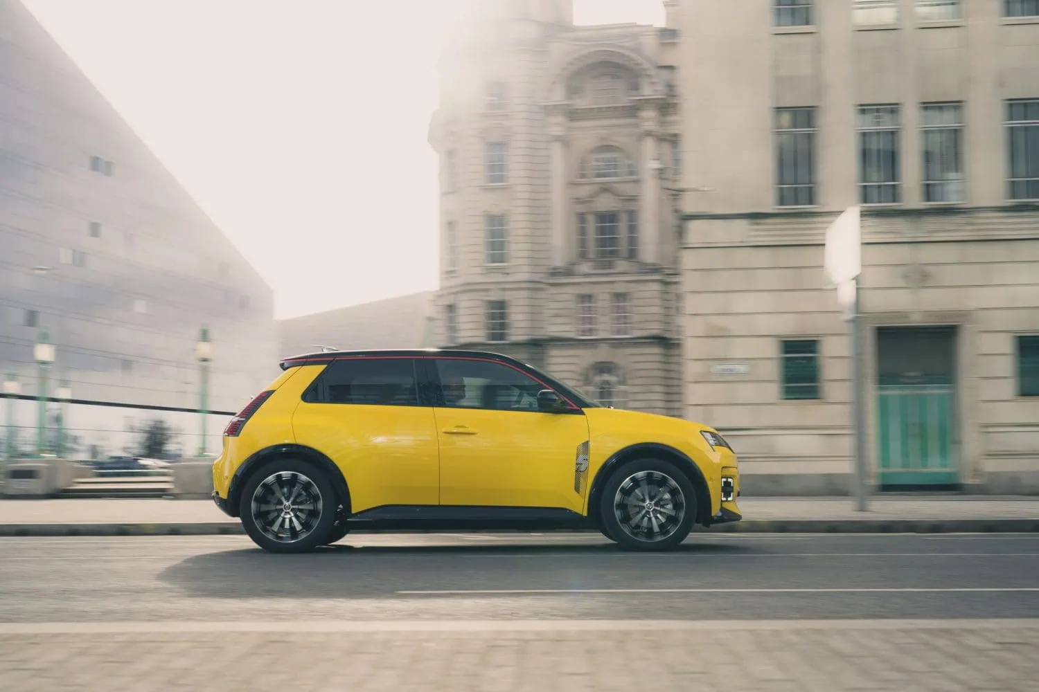 Renault 5 E-Tech electric side profile driving past buildings - Saffarazzi Renault 5 E-Tech electric side profile driving past buildings