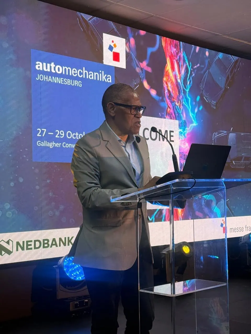 Speaker with Automechanika backdrop - Saffarazzi Speaker at podium before Automechanika Johannesburg branded screen.
